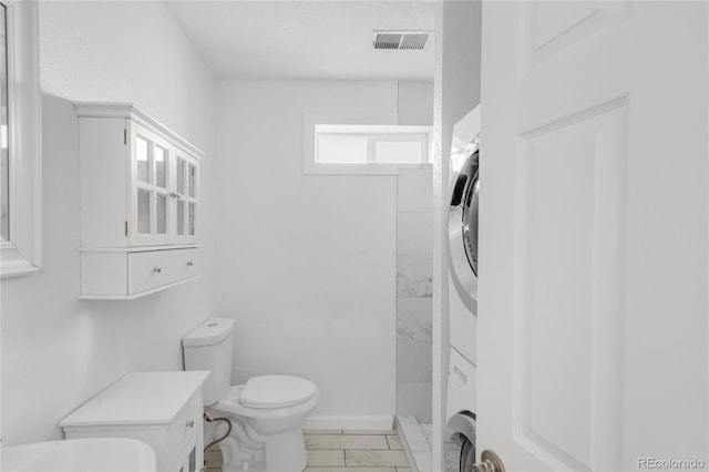 bathroom with toilet, stacked washing maching and dryer, a shower, and tile patterned floors