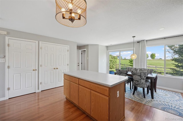 7977 Emerson Ave, Frederick, CO 80530 - kitchen featuring wood finished floors, a center island, a chandelier, light countertops, and hanging light fixtures