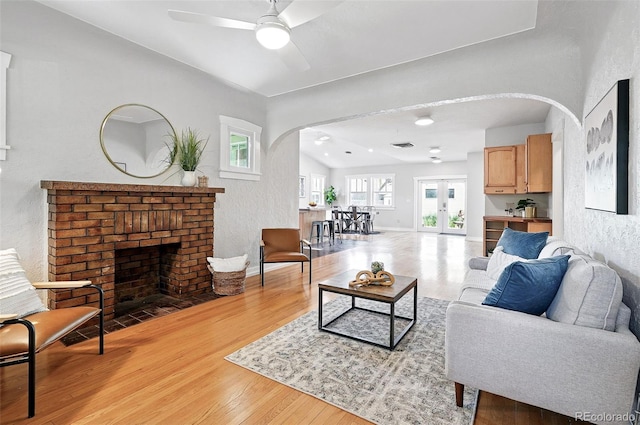 3321 Stuart St, Denver, CO 80212 - living room featuring arched walkways, light wood finished floors, a ceiling fan, a brick fireplace, and french doors