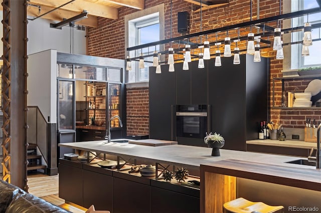 kitchen with sink, a high ceiling, wall oven, brick wall, and beamed ceiling