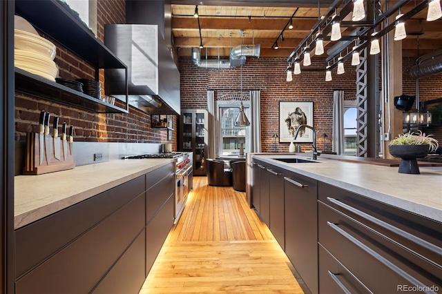 kitchen with high end range, brick wall, sink, and light wood-type flooring