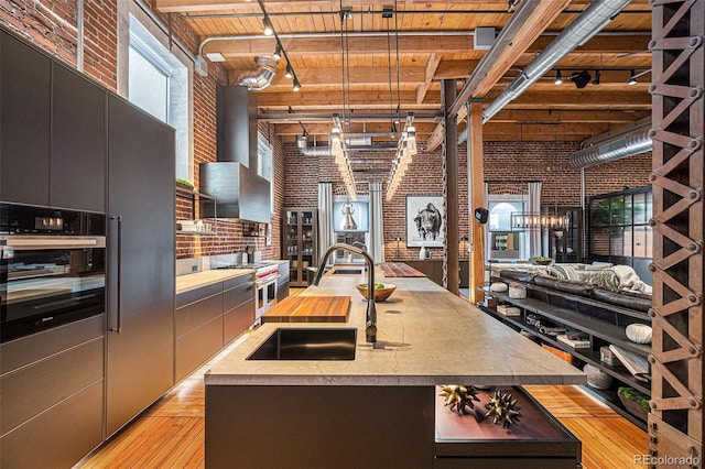 kitchen with pendant lighting, sink, a kitchen island with sink, brick wall, and range with two ovens