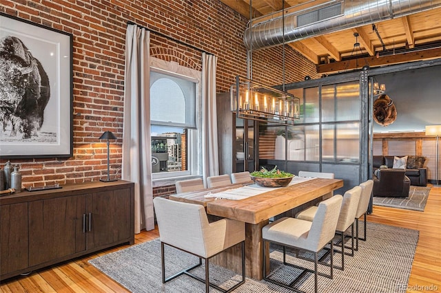 dining room featuring a towering ceiling, light hardwood / wood-style floors, and brick wall