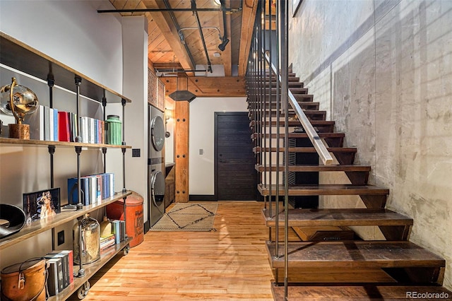 stairs featuring beamed ceiling, wood-type flooring, stacked washer / drying machine, and a towering ceiling