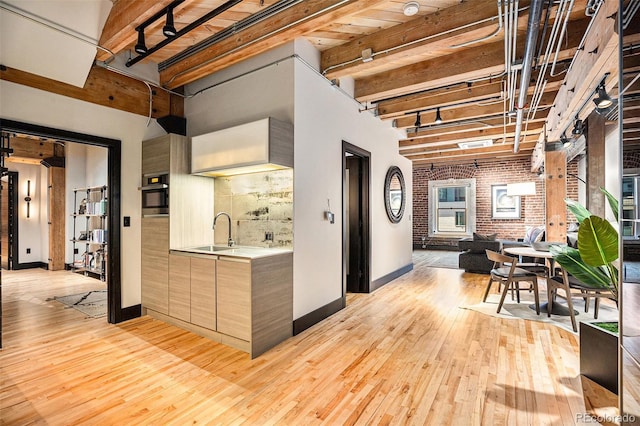 kitchen featuring sink, stainless steel oven, light hardwood / wood-style floors, brick wall, and beamed ceiling