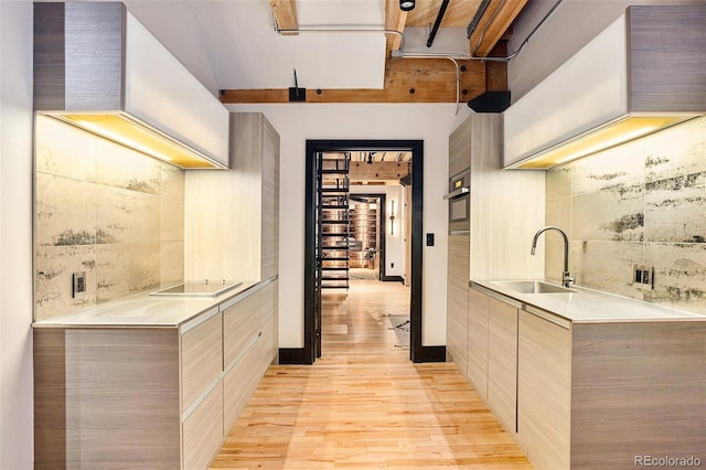 kitchen featuring sink, black electric stovetop, decorative backsplash, oven, and light wood-type flooring