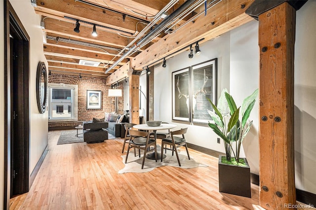 dining space with brick wall, rail lighting, and wood-type flooring