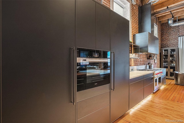 kitchen with brick wall, high end stainless steel range oven, a high ceiling, wall oven, and wall chimney range hood