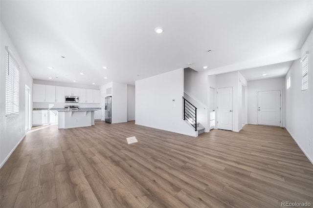 3869 N Shawnee St, Aurora, CO 80019 - unfurnished living room with stairway, light wood-style floors, recessed lighting, and baseboards
