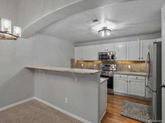 7131 S Wenatchee Way Unit C, Aurora, CO 80016 - kitchen with appliances with stainless steel finishes, white cabinetry, a kitchen bar, light stone counters, and a peninsula