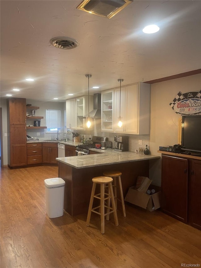 kitchen featuring kitchen peninsula, a kitchen bar, light wood-type flooring, stainless steel gas range, and white cabinetry