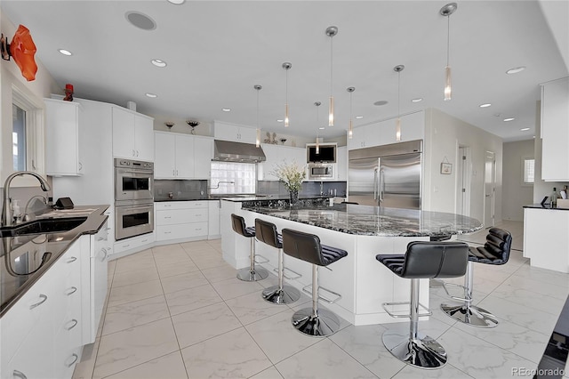 kitchen featuring a spacious island, sink, built in appliances, dark stone countertops, and white cabinets