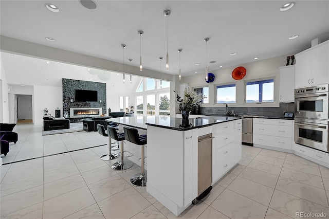 kitchen with a kitchen island, double oven, decorative light fixtures, a large fireplace, and white cabinetry