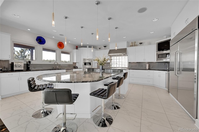 kitchen featuring ventilation hood, a spacious island, sink, built in appliances, and white cabinetry