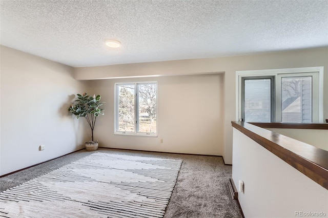 empty room featuring light carpet, a textured ceiling, and baseboards