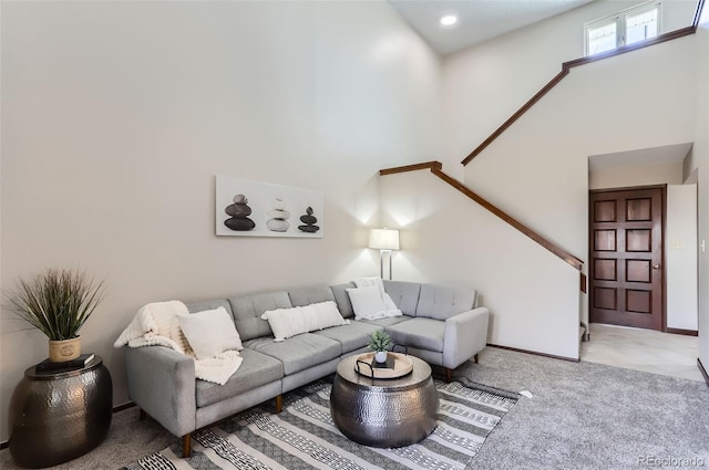 living area with a towering ceiling, baseboards, and light colored carpet