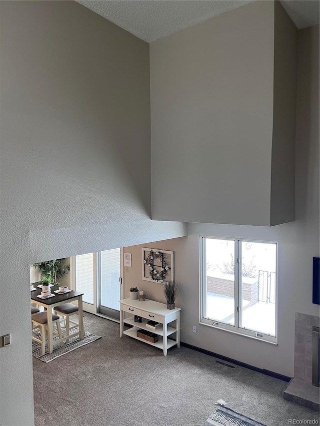 living area featuring carpet floors, a high ceiling, visible vents, and a fireplace with raised hearth