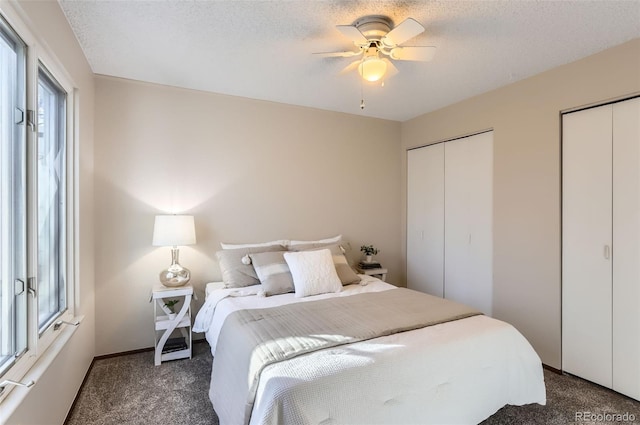 bedroom with a ceiling fan, dark carpet, a textured ceiling, and two closets