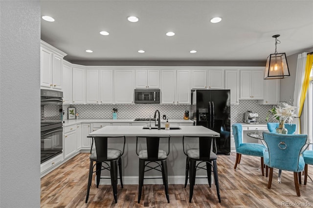 24682 E Ontario Dr, Aurora, CO 80016 - kitchen featuring black appliances, tasteful backsplash, a center island with sink, wood finished floors, and white cabinetry
