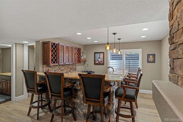 24682 E Ontario Dr, Aurora, CO 80016 - indoor wet bar featuring light wood-style floors, baseboards, a textured ceiling, and decorative light fixtures
