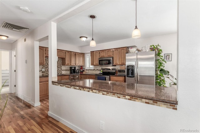 kitchen with decorative backsplash, appliances with stainless steel finishes, dark wood-type flooring, pendant lighting, and dark stone countertops