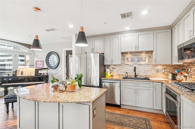 kitchen with a center island, backsplash, sink, appliances with stainless steel finishes, and decorative light fixtures