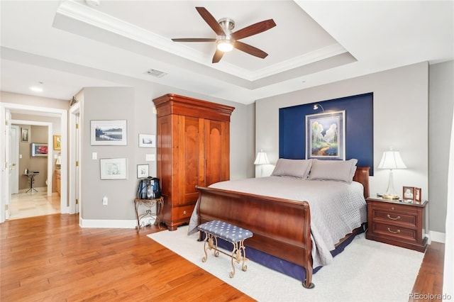 bedroom with ornamental molding, a tray ceiling, ceiling fan, and light hardwood / wood-style floors