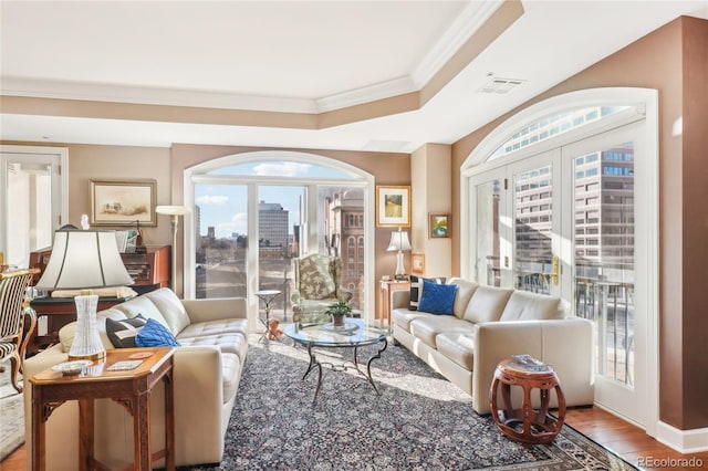 living room with hardwood / wood-style flooring, a raised ceiling, plenty of natural light, and crown molding