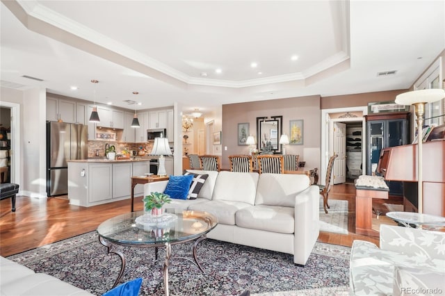 living room with light hardwood / wood-style flooring, a raised ceiling, and crown molding