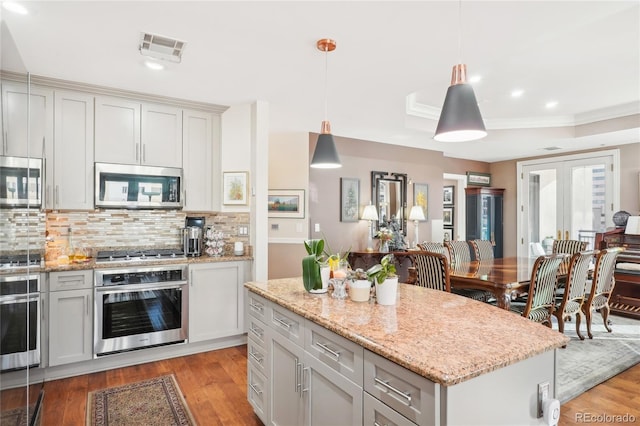 kitchen featuring appliances with stainless steel finishes, light wood-type flooring, tasteful backsplash, pendant lighting, and a center island