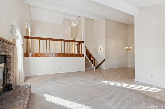 unfurnished living room with ceiling fan with notable chandelier, a brick fireplace, light colored carpet, and high vaulted ceiling