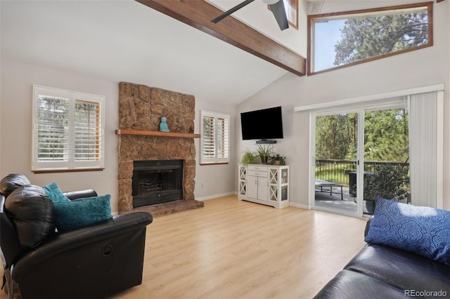 living room with ceiling fan, light hardwood / wood-style flooring, a stone fireplace, and lofted ceiling with beams