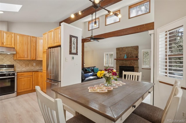 kitchen featuring stove, vaulted ceiling with skylight, ceiling fan, a fireplace, and stainless steel refrigerator