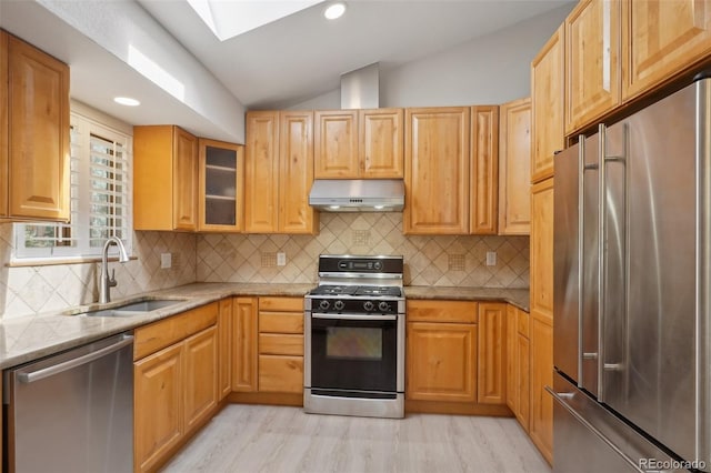 kitchen featuring appliances with stainless steel finishes, light hardwood / wood-style floors, light stone countertops, vaulted ceiling with skylight, and sink