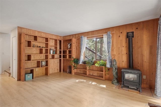 living area with a wood stove, light hardwood / wood-style flooring, and wooden walls