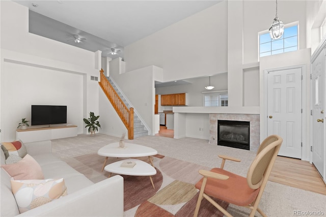 living room featuring a towering ceiling, a tiled fireplace, ceiling fan with notable chandelier, and light carpet