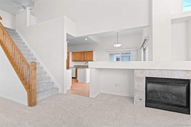 kitchen featuring light colored carpet, white dishwasher, a tile fireplace, and a towering ceiling