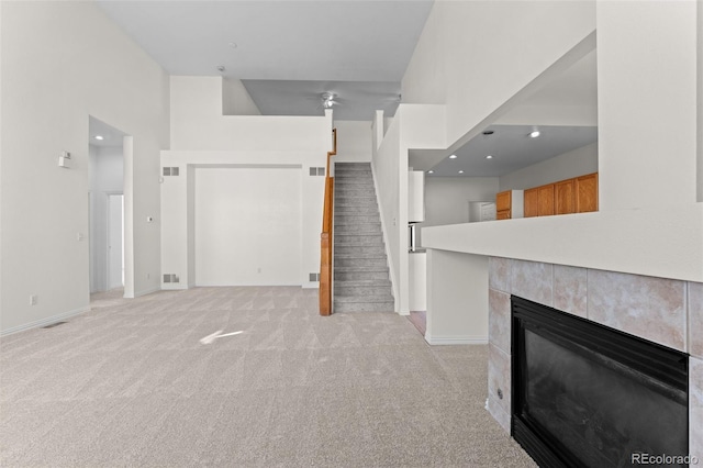 unfurnished living room with a tile fireplace, a towering ceiling, and light colored carpet