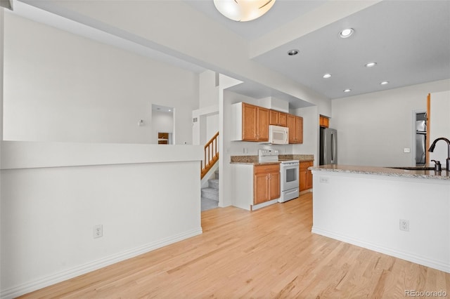 kitchen with light stone countertops, sink, white appliances, and light wood-type flooring