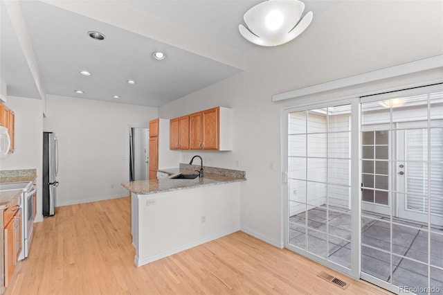 kitchen with white electric range oven, sink, light hardwood / wood-style flooring, stainless steel refrigerator, and light stone countertops