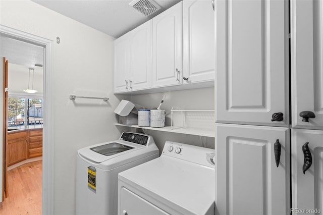 washroom with independent washer and dryer, wood-type flooring, and cabinets