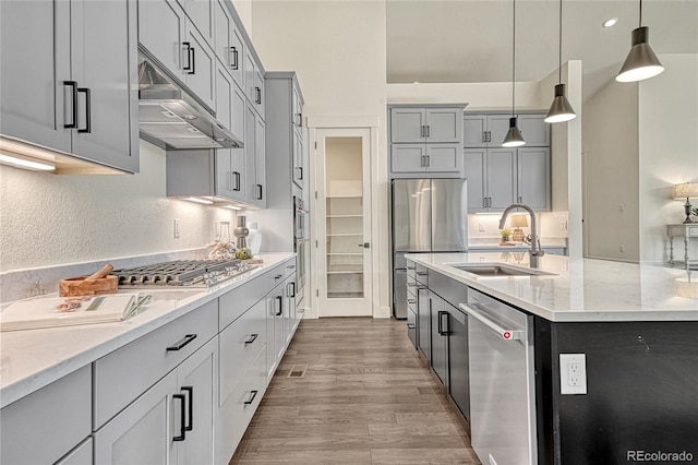 kitchen with sink, hanging light fixtures, hardwood / wood-style flooring, light stone counters, and stainless steel appliances