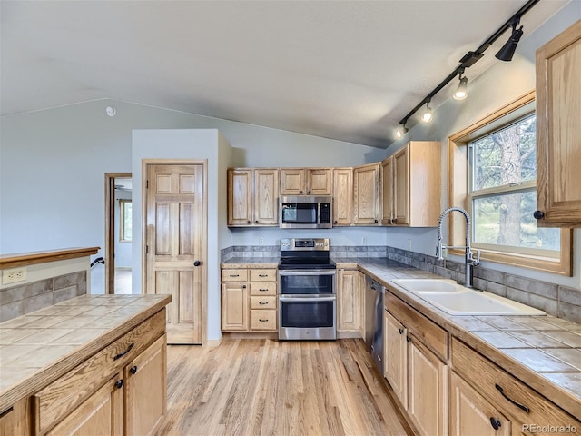 kitchen featuring stainless steel appliances, light hardwood / wood-style floors, rail lighting, sink, and vaulted ceiling