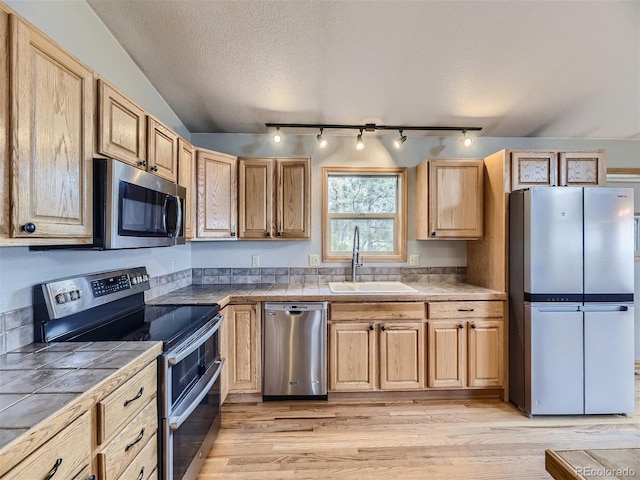 kitchen with sink, appliances with stainless steel finishes, rail lighting, light hardwood / wood-style floors, and a textured ceiling