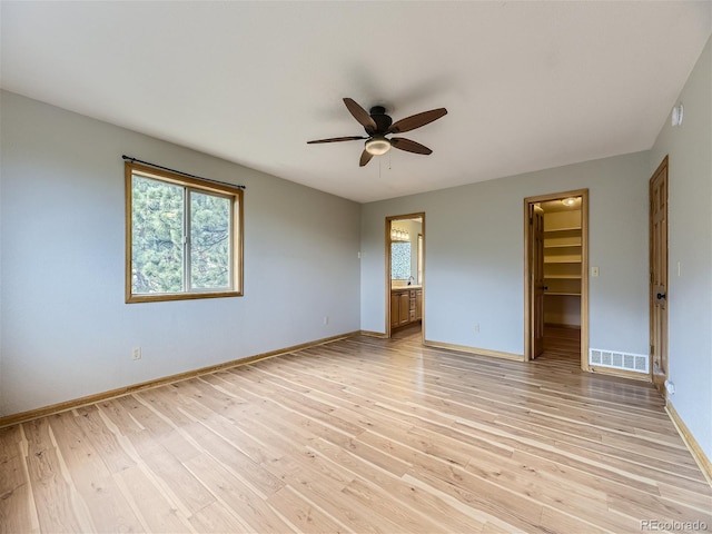 unfurnished bedroom featuring light hardwood / wood-style flooring, a spacious closet, a closet, ceiling fan, and connected bathroom