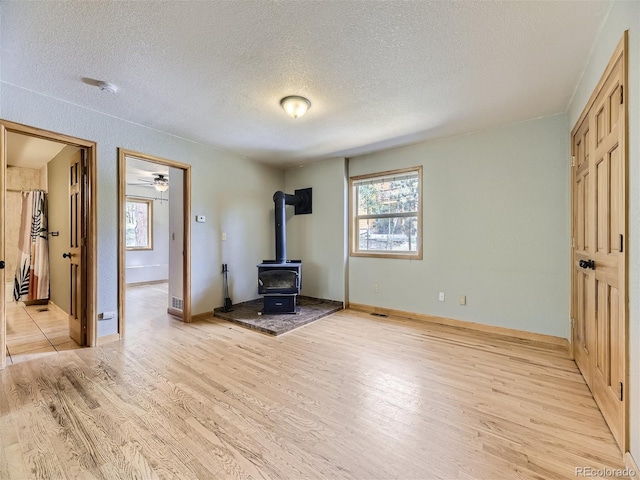 unfurnished bedroom featuring a textured ceiling, light hardwood / wood-style flooring, a wood stove, and ensuite bathroom