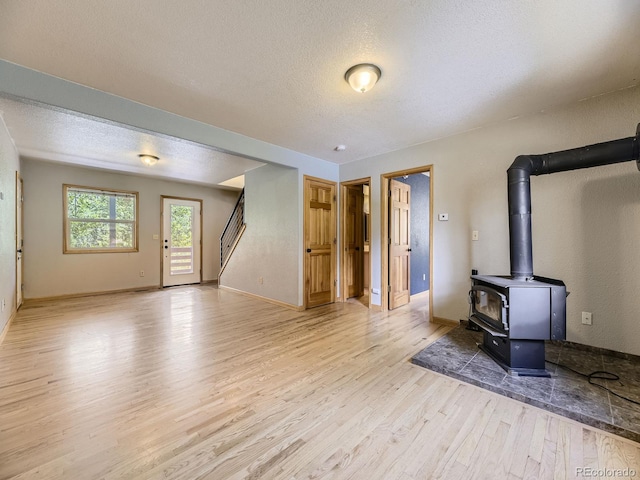 unfurnished living room with light wood-type flooring, a wood stove, and a textured ceiling