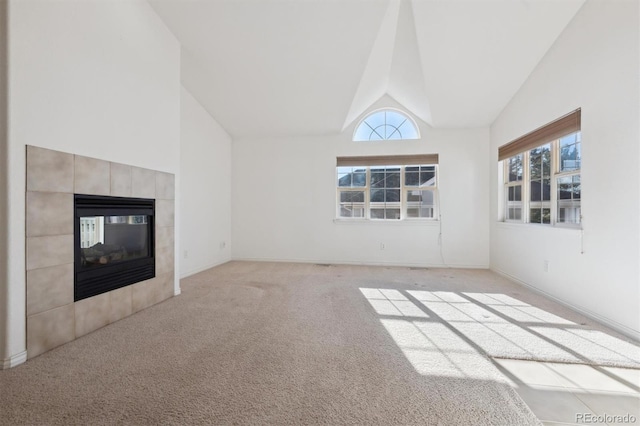 unfurnished living room with a tile fireplace, light carpet, high vaulted ceiling, and a healthy amount of sunlight