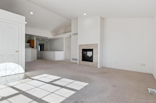 unfurnished living room with a tile fireplace, light colored carpet, and high vaulted ceiling