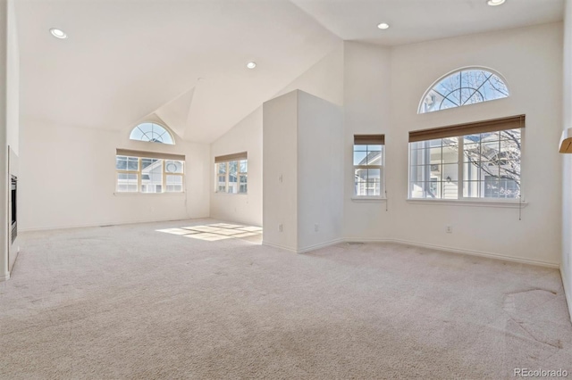 unfurnished living room with high vaulted ceiling and light colored carpet